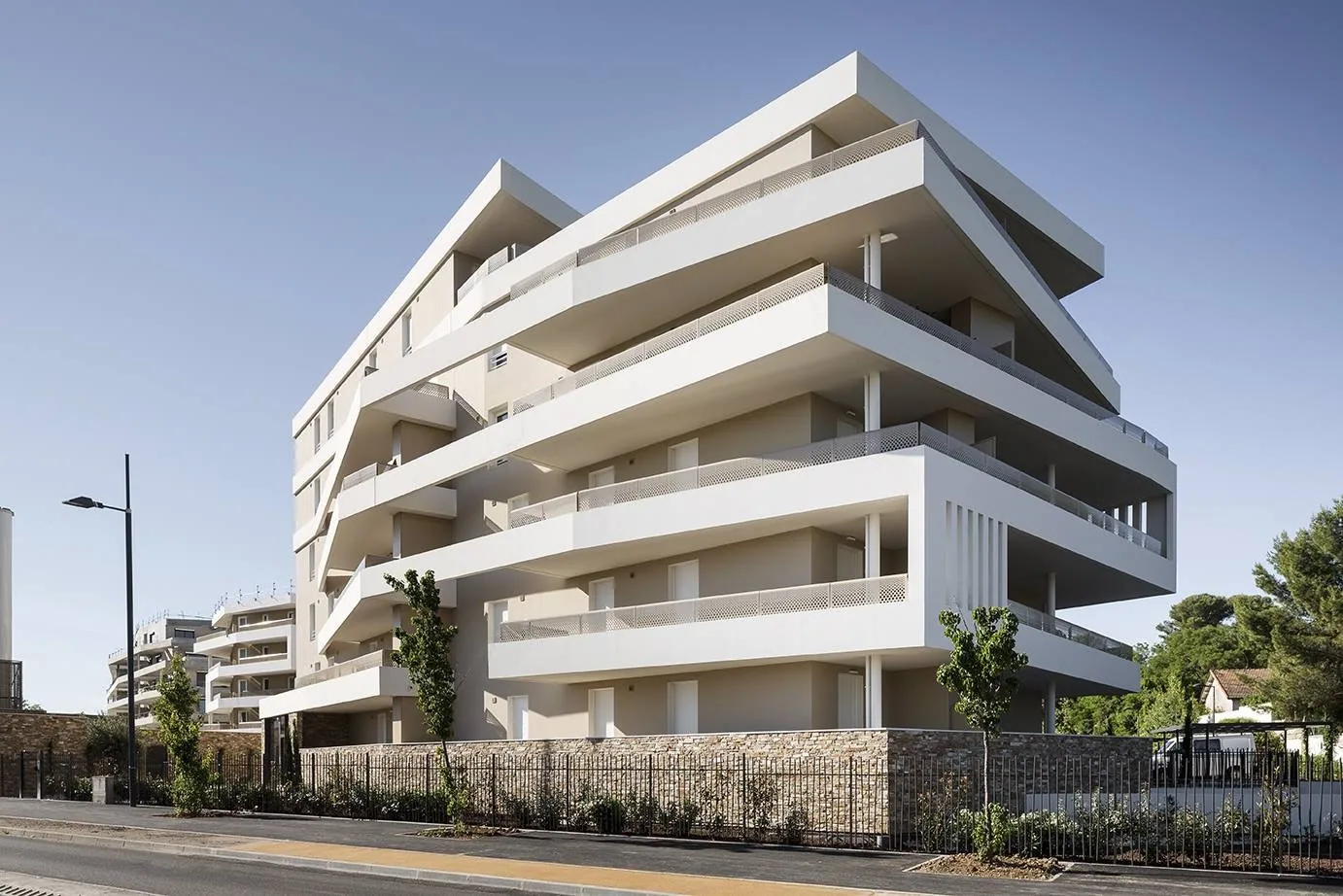 Programme de logements collectifs, volumes blancs et soubassement minéral